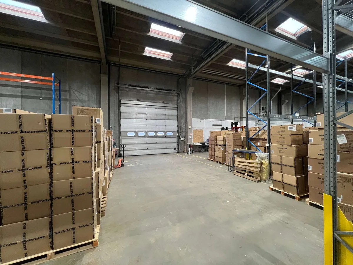 Lager med flere kartoner, der indeholder Skechers. Højt gulv med store åbninger og skyggefuldt lys.