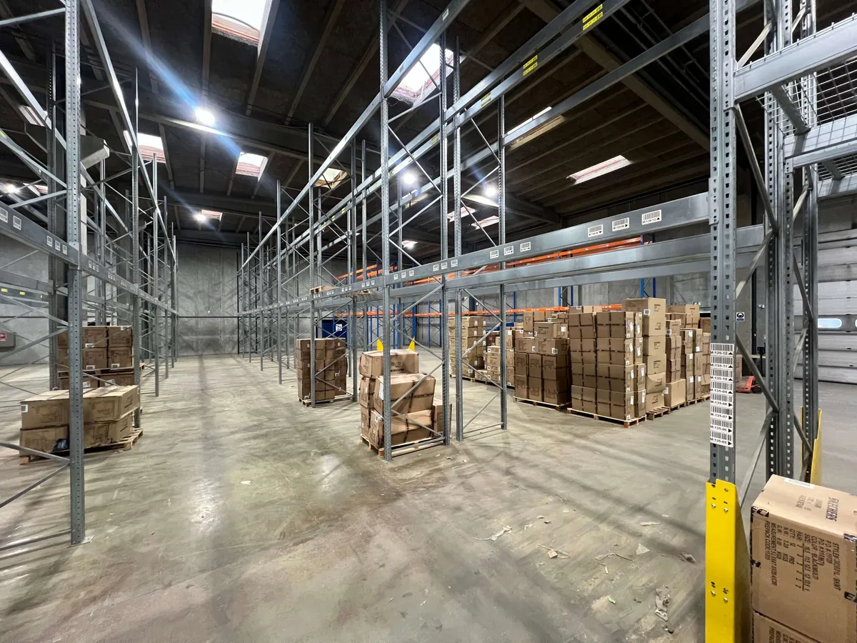 Lager med flere rækker med stel og lagerkasser i Esbjerg. Stengulv med højtloft og lyser.