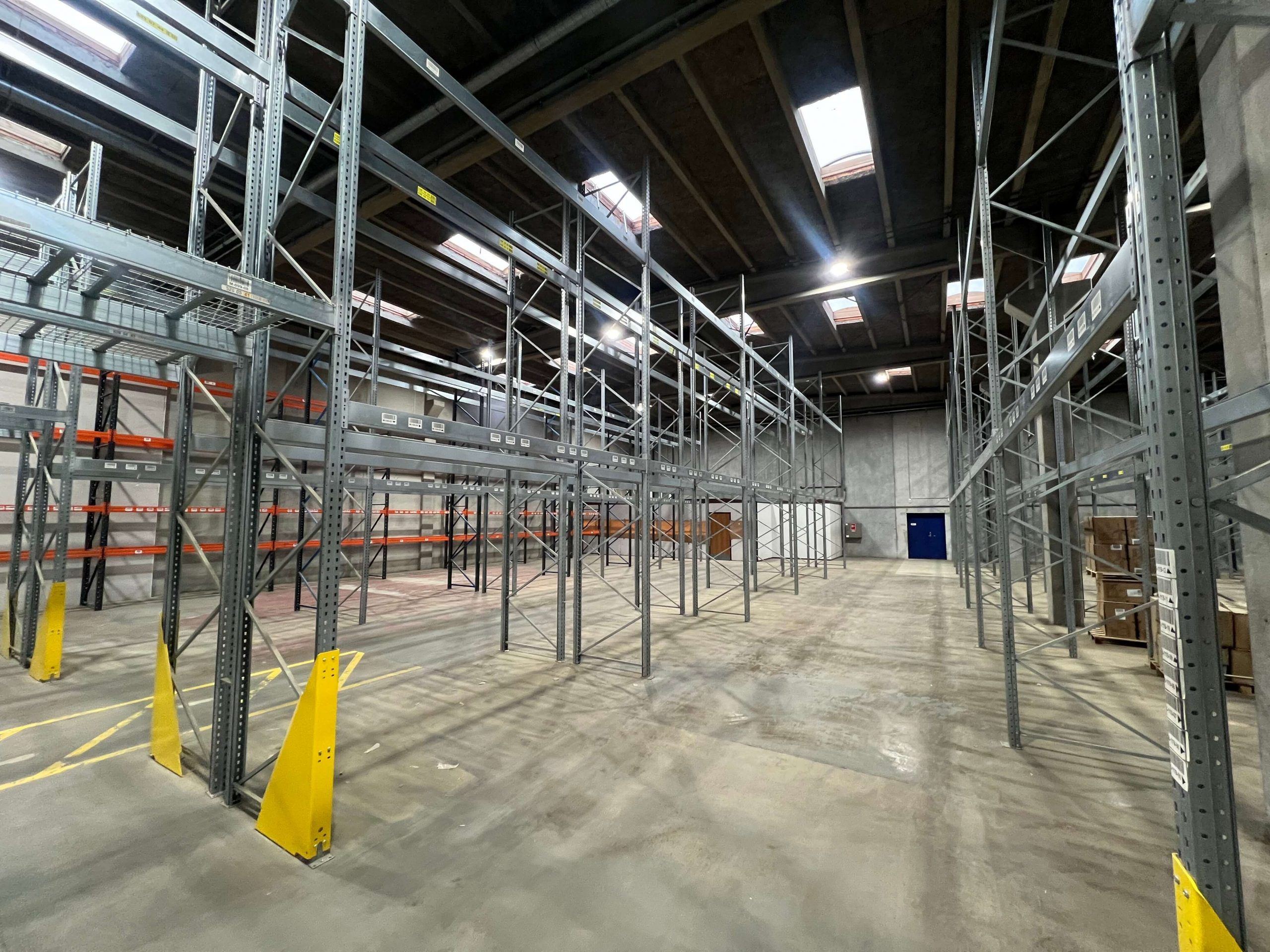 Lager med metalreoler og kasser i en stor lagerhal med højloft og flere skylys