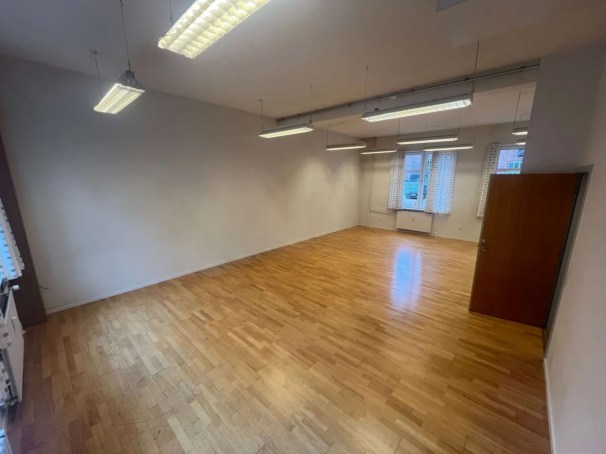 Lejlighed med åben rum, lysegule vægge, lysegrå loft og lysgrå gulv. Der er fire lysekroner hængende og trægulv i et hjørne.