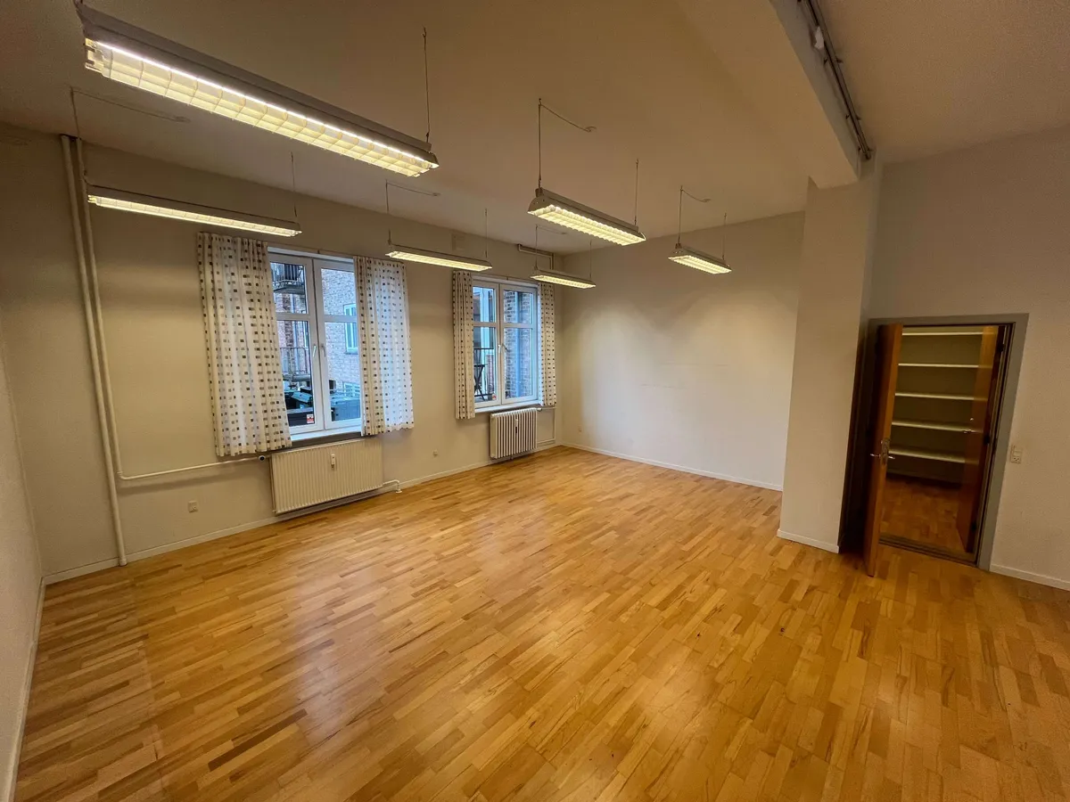 En tom og lys erhvervslejlighed med store vinduer, hvide vægge og lyse loftslamper. Lejligheden er let og rummelig med