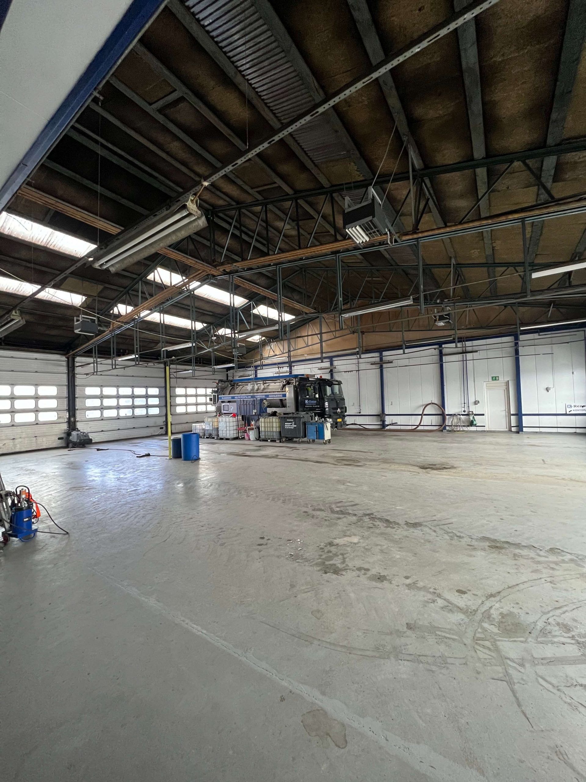 En stor, ren, tom lagerhal med høje lofter og mange store, lyseruderede garageporte. Der er flere køretøjer og