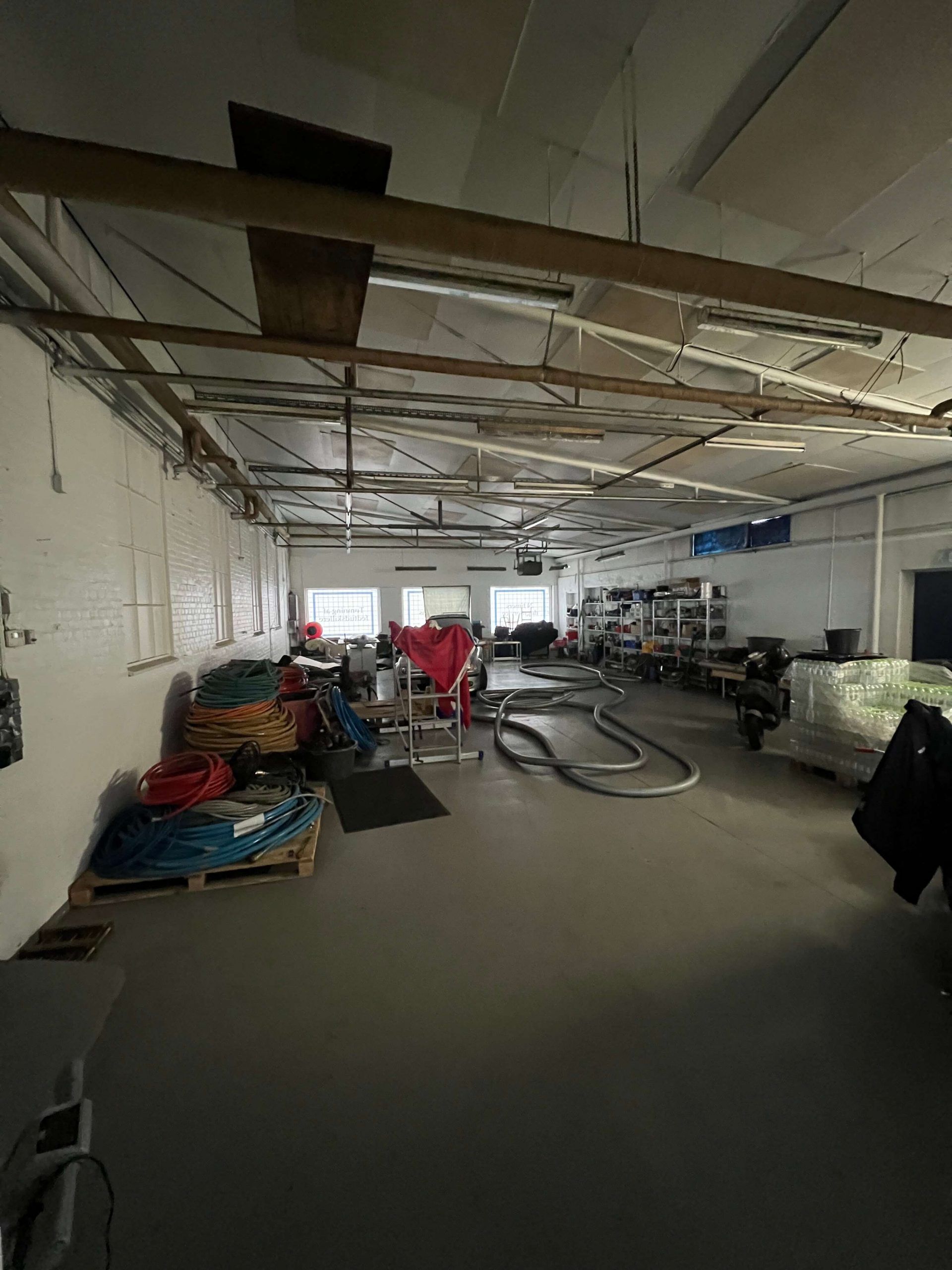 En stor lagerhal med røde, orange, og blå slanger samt diverse lagermateriale og vægmontered hylder