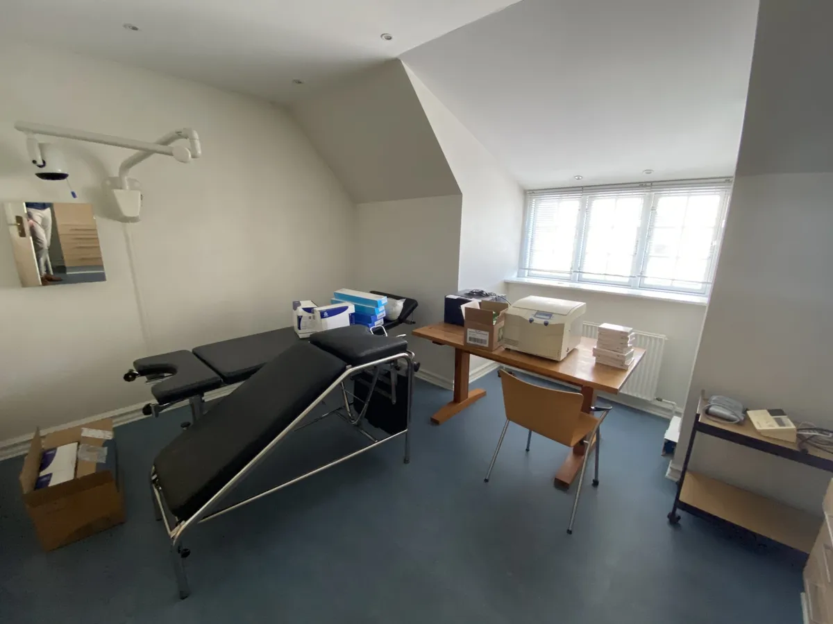 En lægepraksis med en lægestol, en bord, et lille køleskab og en boks med papirkasser samt et spejl med en refleksion af en