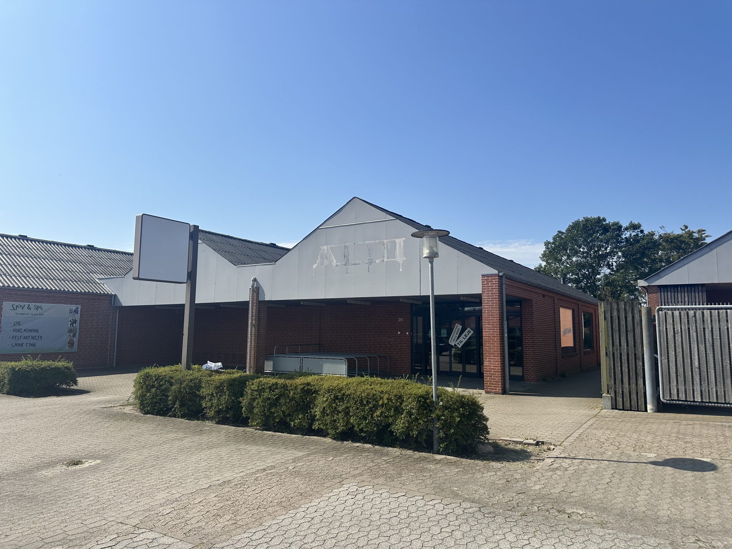 En rødmalet murstensbygning med nummer 20 på facaden. På facaden er der et reklameskilt med teksten Snow & Spil. Der er et