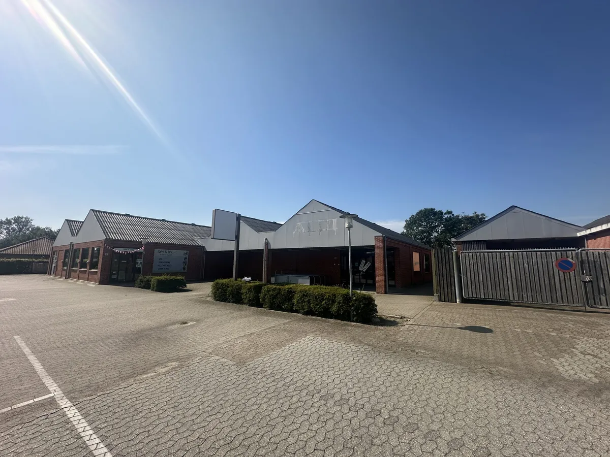 En stor bygning med røde mursten og stående skilt med tekst og nummer 20, ligesom der er en lysstang og en stor buskehæk