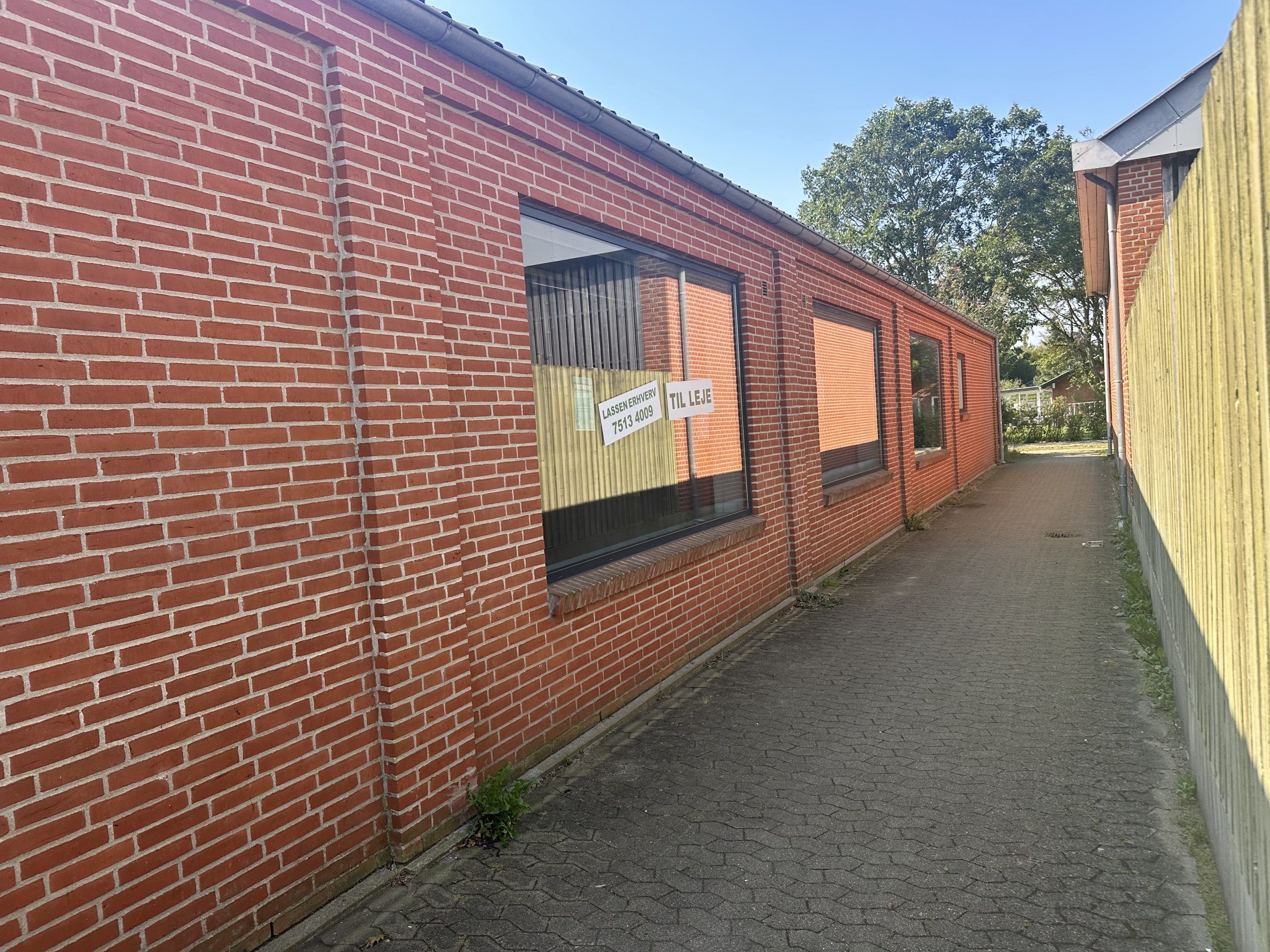 En rødmalet murstensbygning med vinduer og skilte og en brolagt stien til højre for bygningen