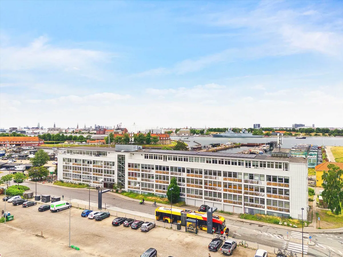 En luftfoto af en bygning med mange vinduer, et busstoppested og parkerede biler og busser