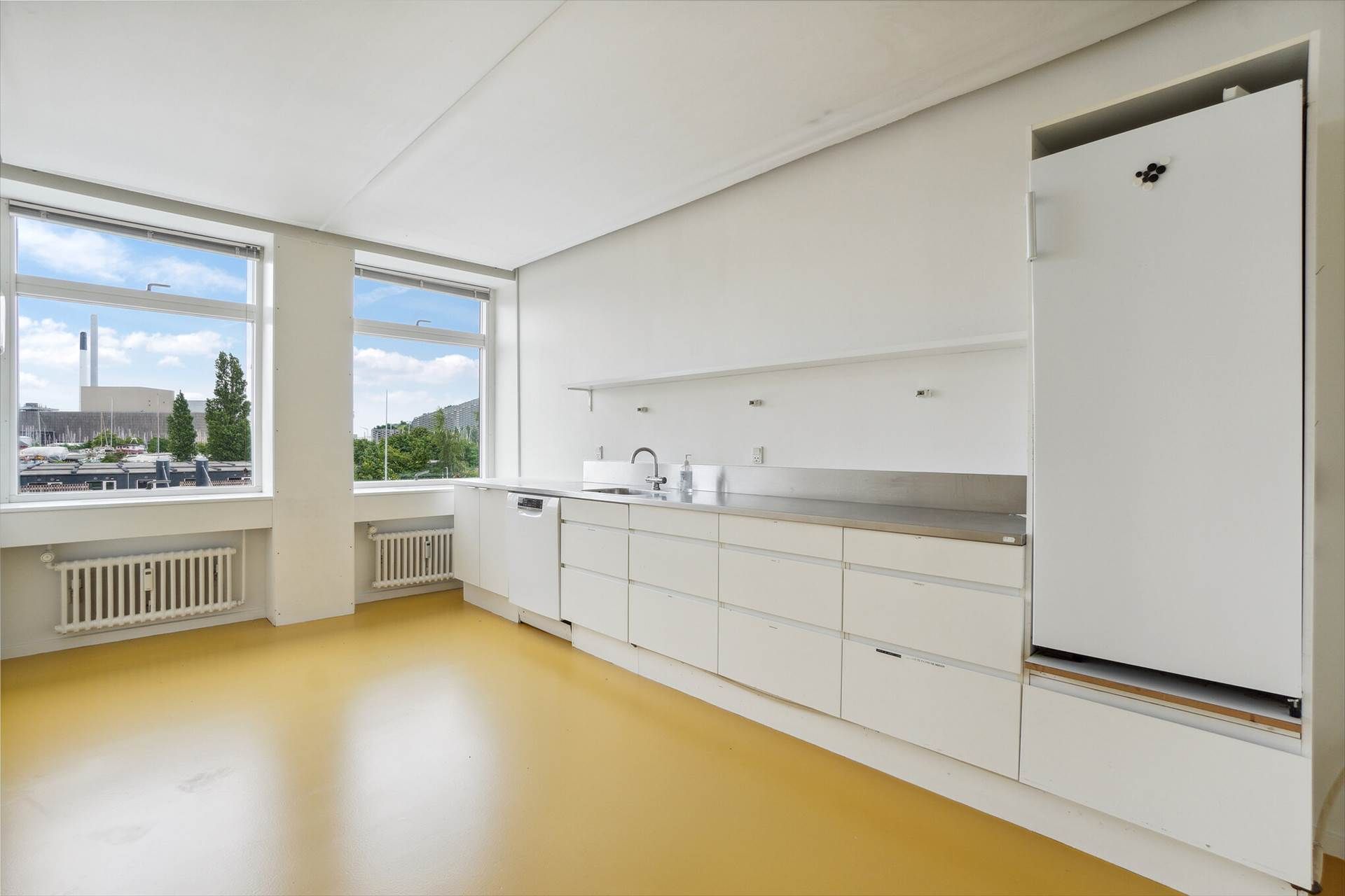 En moderne køkken med hvide vægge og gulv, hvidt køkkenskab og rustfrit stål og et køleskab med knapper og magneter