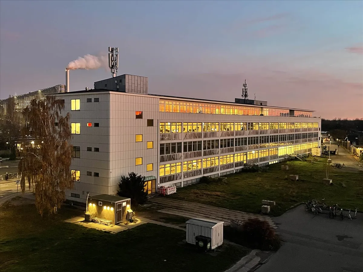 Et stort bygningskompleks med flere etager og lyse vinduer, der er belyst indefra. Der er en mindre bygning og en række