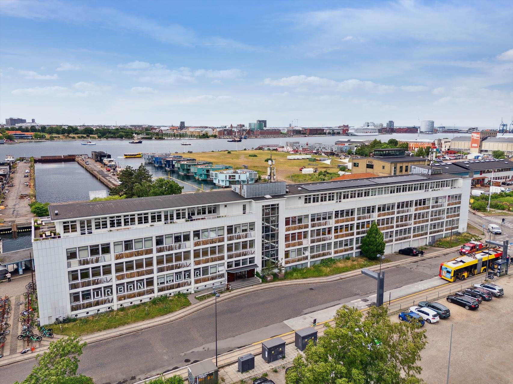 En stor hvid bygning med mange vinduer med teksten Urban Power på facaden og udsigt over en havn med mange skibe