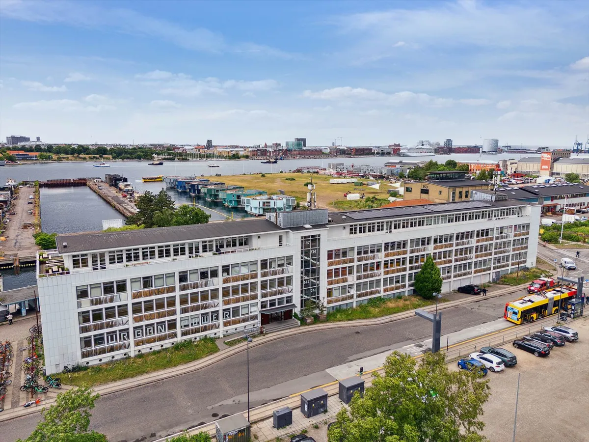 En stor hvid bygning med mange vinduer med teksten Urban Power på facaden og udsigt over en havn med mange skibe