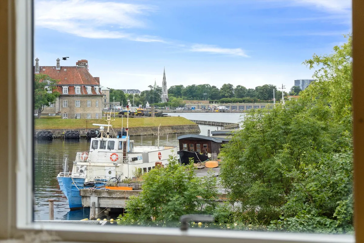 En lys stue med udsigt over Havneløbet og Kastellet med udsigt til havnen, hvor skibe er ankret ved kajen