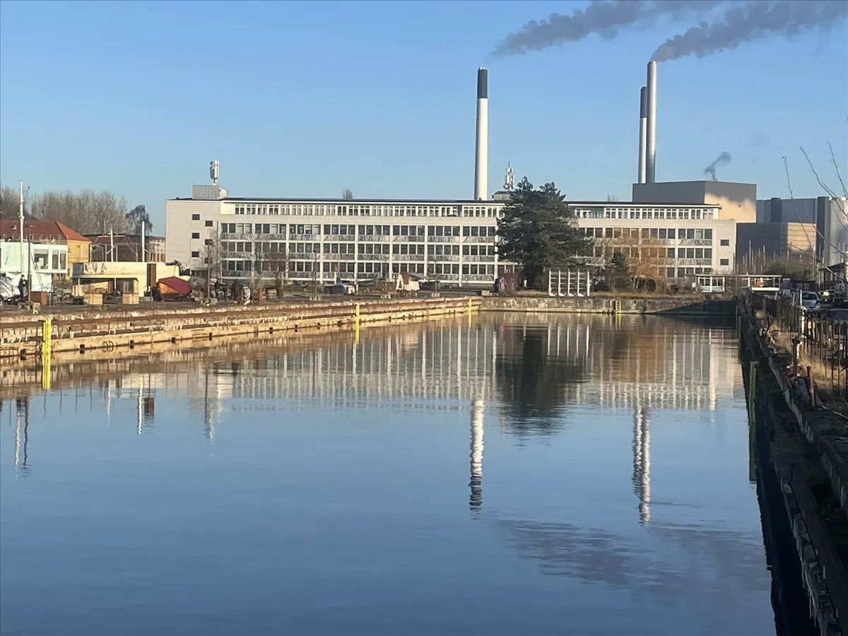 Moderne bygning med to røgudstødende skorstene, en stor vandmasse og refleksioner af bygningen i vandet