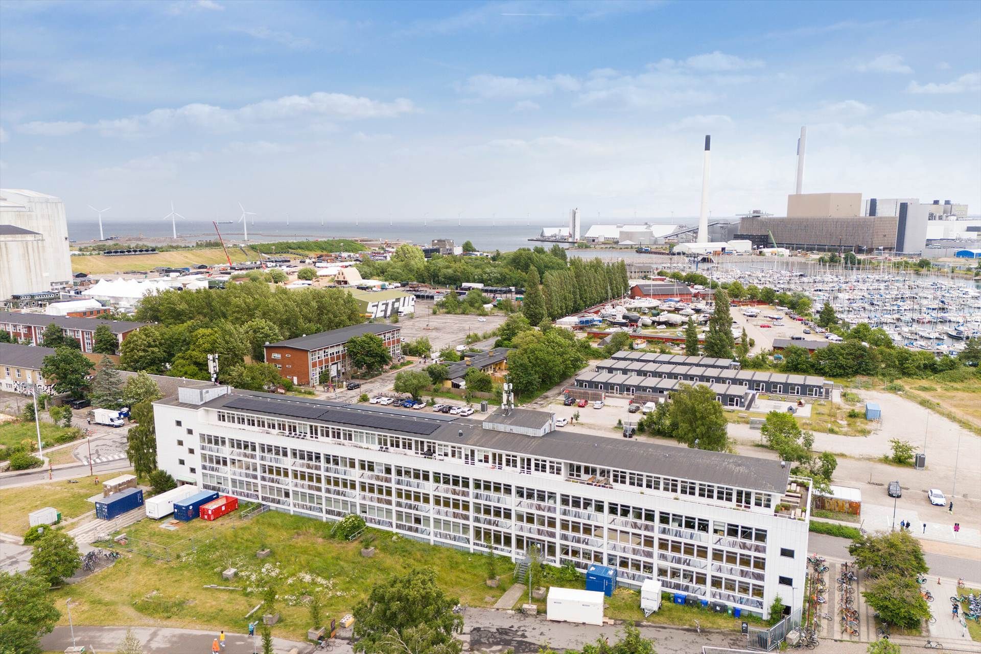 Bygning med solceller og udsigt over byen og marinaen med mange både, vindmøller og industri.