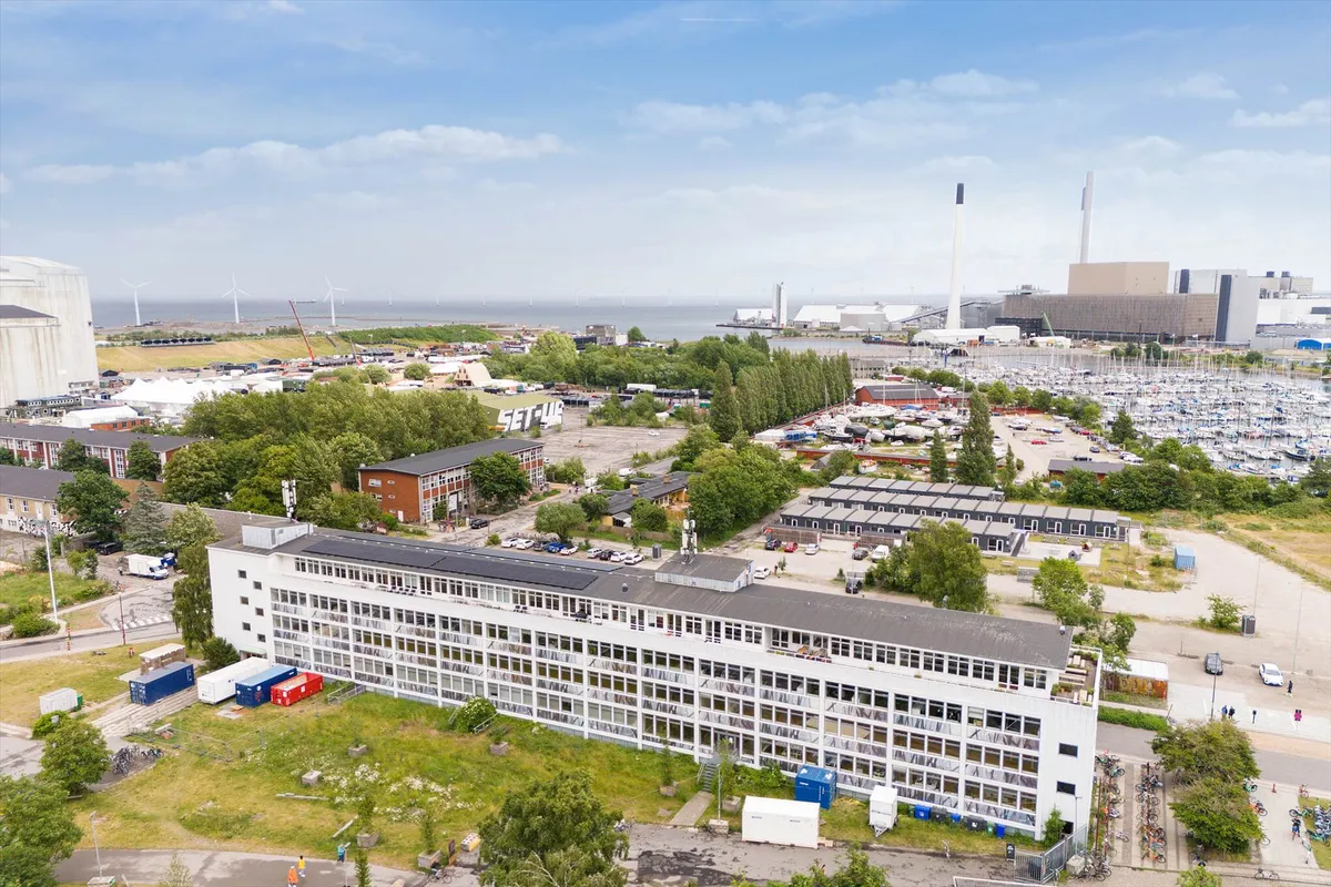 Bygning med solceller og udsigt over byen og marinaen med mange både, vindmøller og industri.