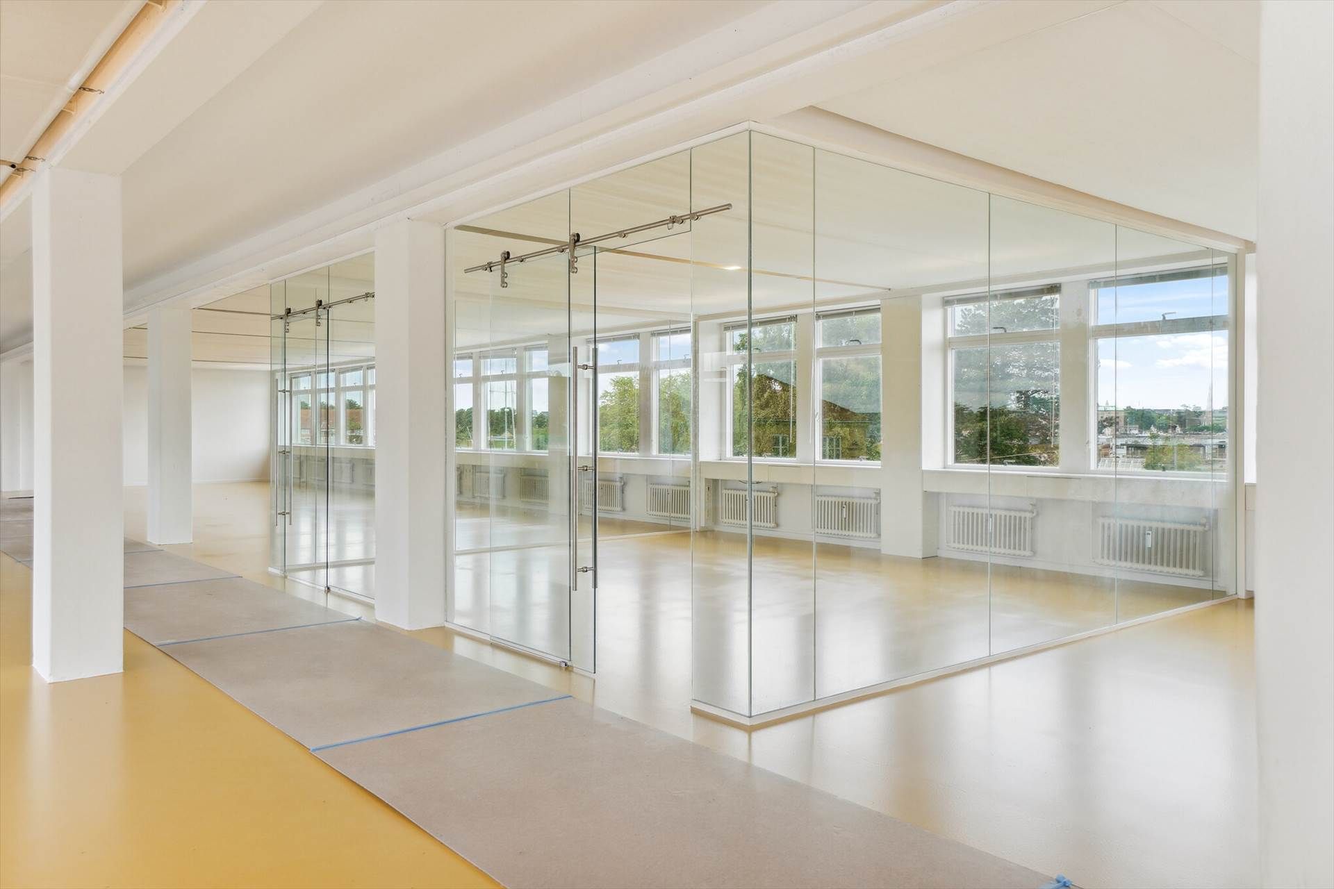 En stor og lys kontorrum med store glasvægge, hvide søjler, højt til loftet, store vinduer og en gulvbelægning med en