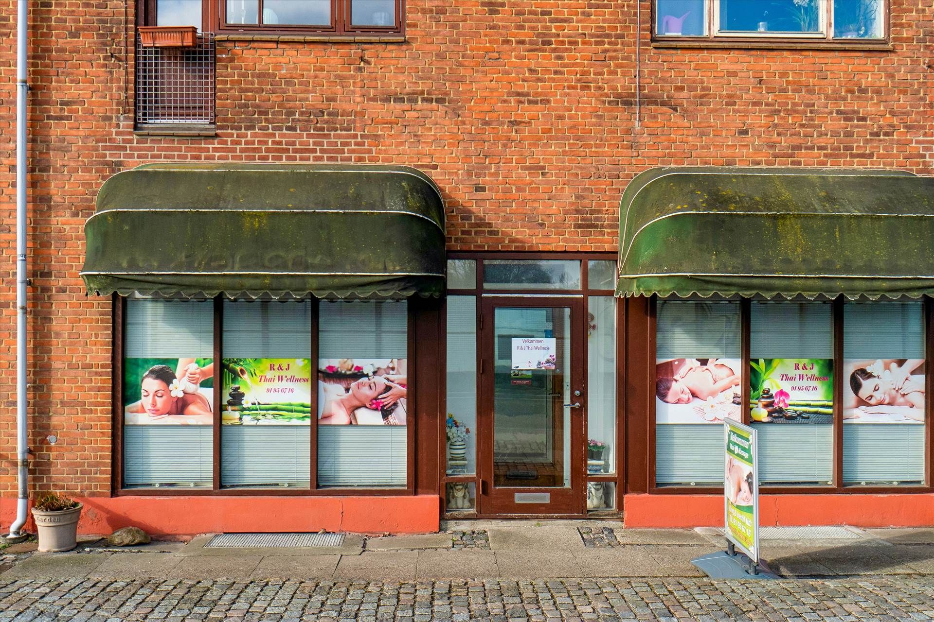 Thai massageklinik med to aulavinduer og reklameplakater, der viser kvinder, der får massage