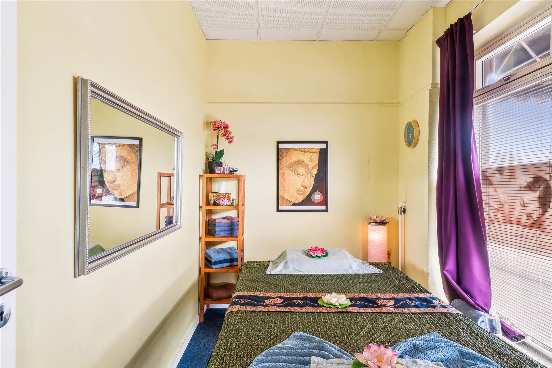 Massageværelse med masser af naturligt lys, blå gardiner og en stor spejl. Et orientalsk værelse med pude, tæppe og