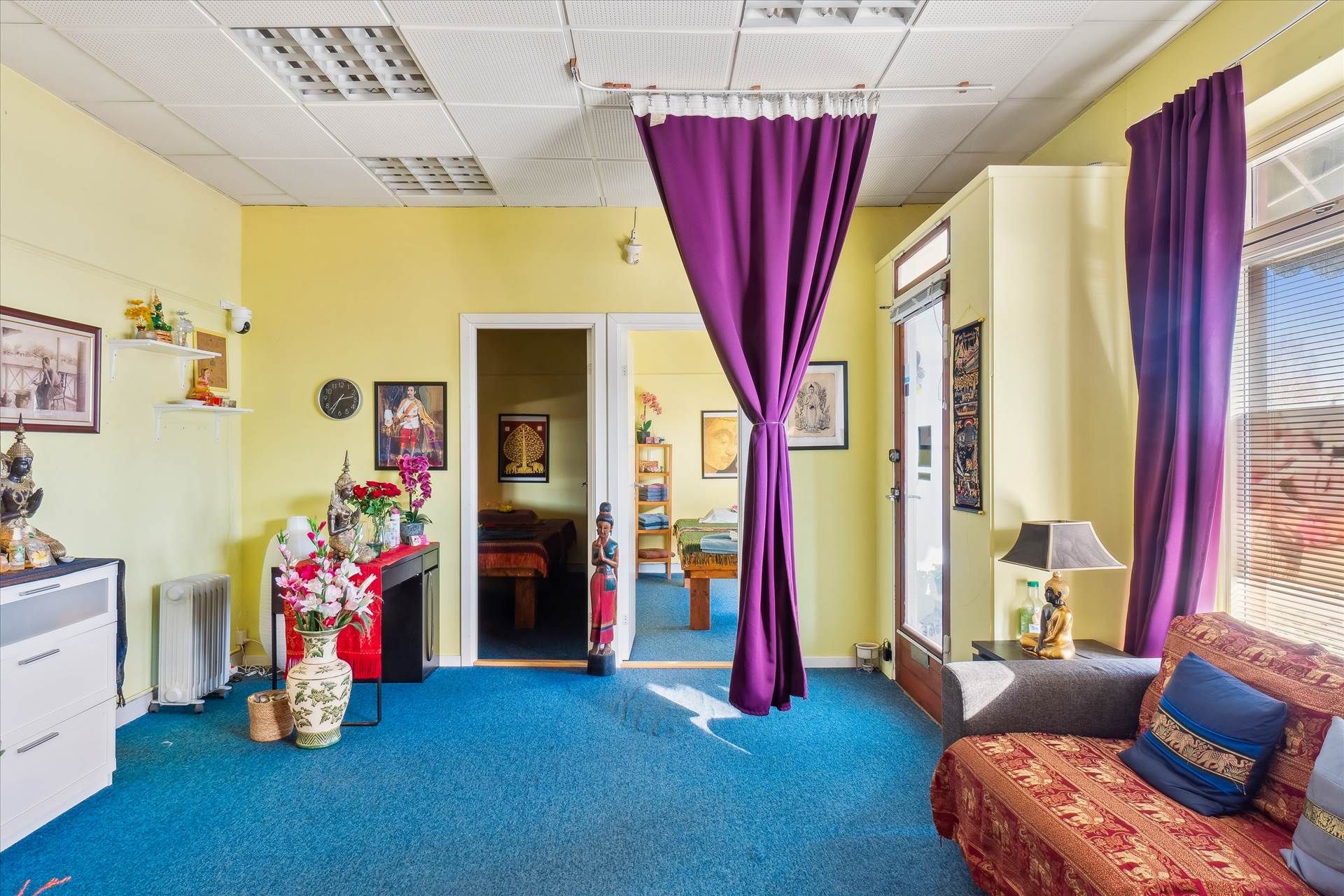 Indretning med blå gulv og gule vægge, gulvtæppe og sofa med tæppe og pude, lysekroner og lampe, kunstværker og statuer,