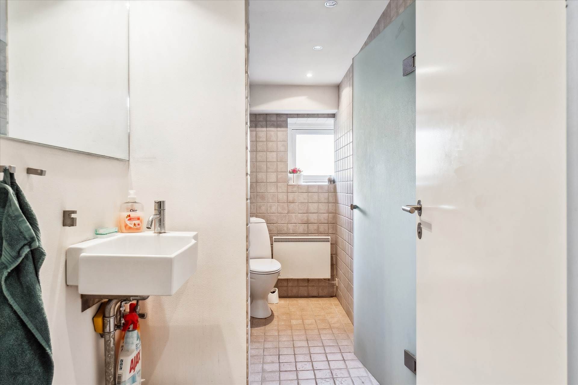 En moderne badeværelse med hvidt toilet, hvidt vasketøj og lysegrå keramiske fliser på gulvet og væggene