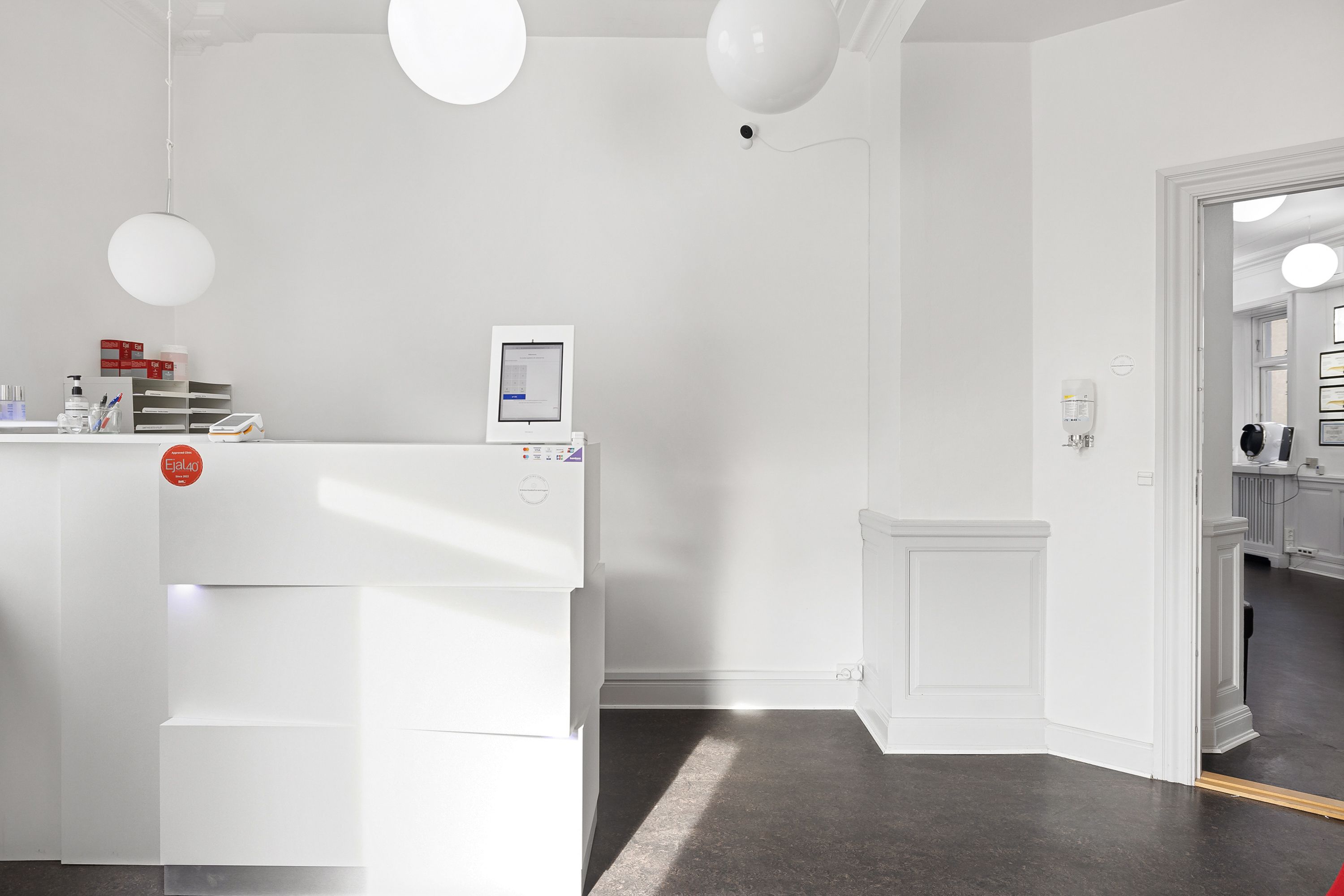 I en ren hvid stue med højt til loftet, hænger runde lampekugler og et monitor er installeret på et bord med en rødmalet