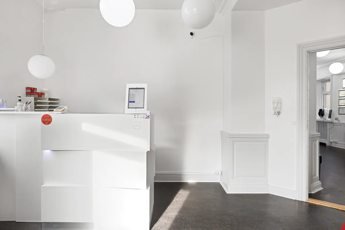 I en ren hvid stue med højt til loftet, hænger runde lampekugler og et monitor er installeret på et bord med en rødmalet