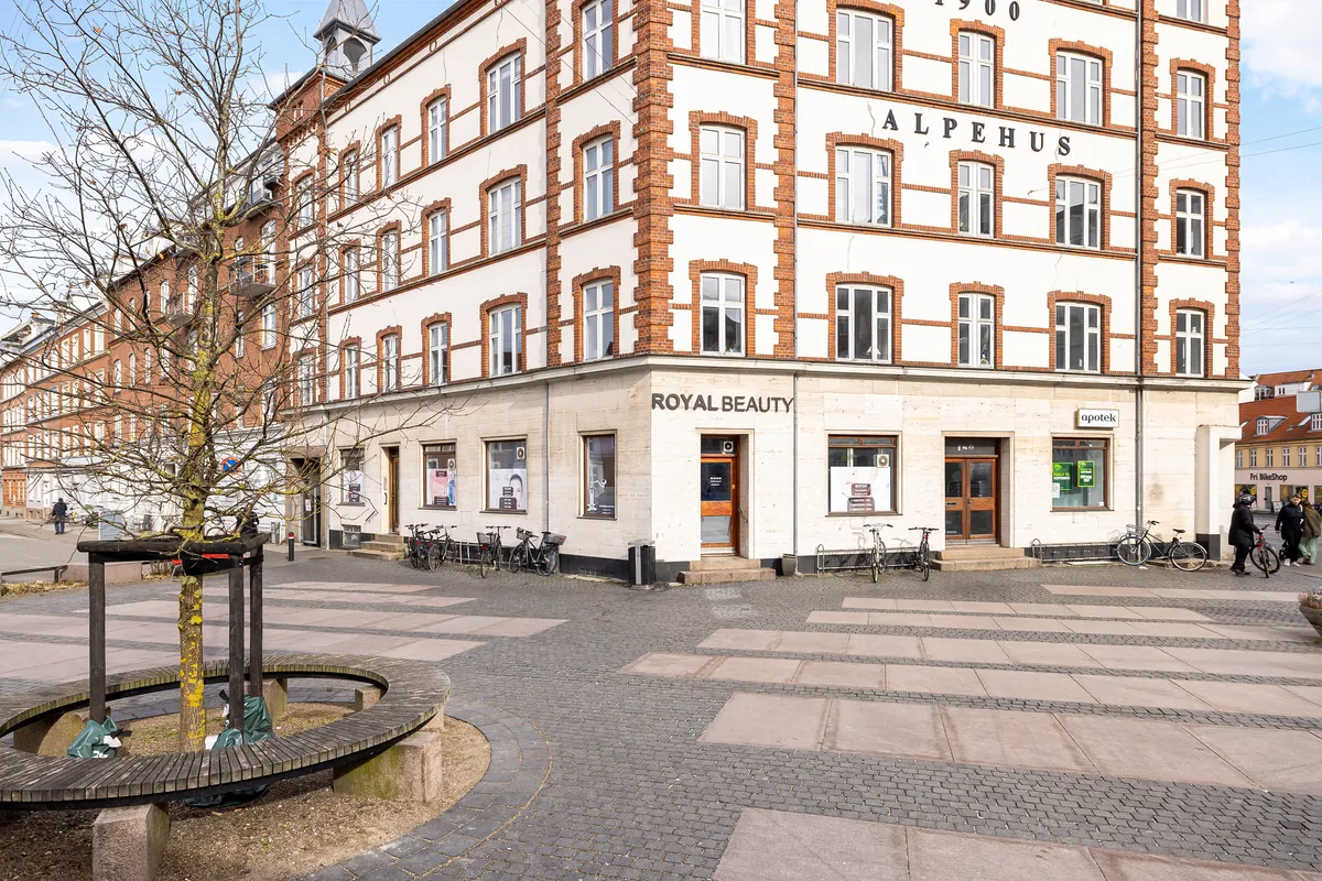 Frederiksbjerg Torv med røde teglstensbygning med butikker og Royal Beauty salon og to cykler parkeret foran