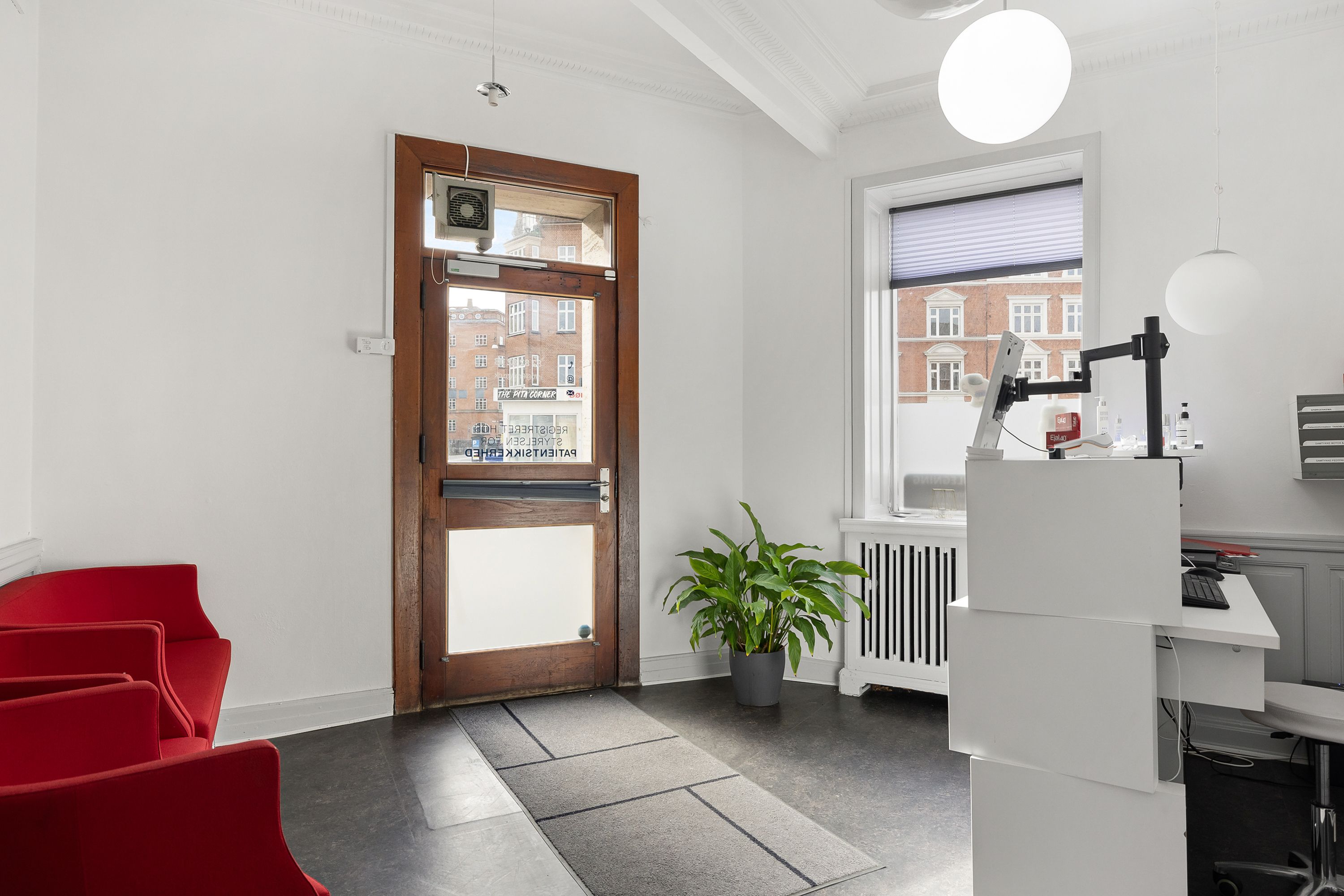 Nydelig kontorlokaler med hvide vægge og moderne møbler, herunder en hvid skranke, en sort stol og røde stole, samt en