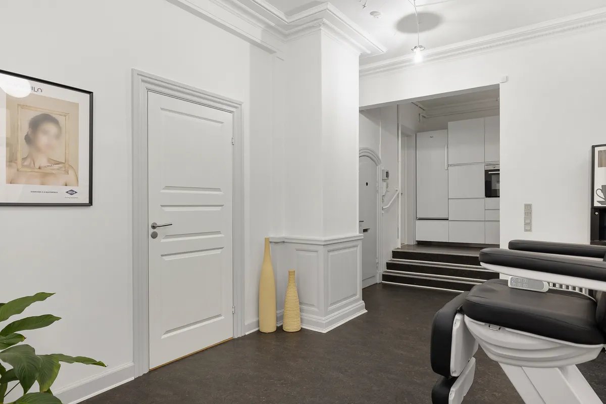 Et moderne interiør med hvide vægge, gulv og loft, hvor der er en hvid dør og en stribet gulvvedligeholder, samt en