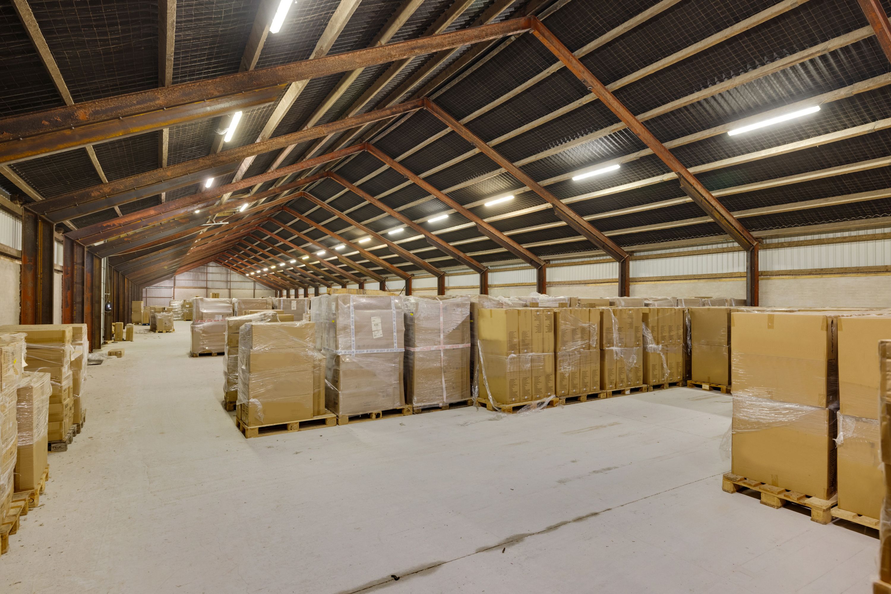 Lagerhal med store lagerkasser på træpæle, stålbjælker og lys. Lofterne er dækket af metal og stålbjælker.