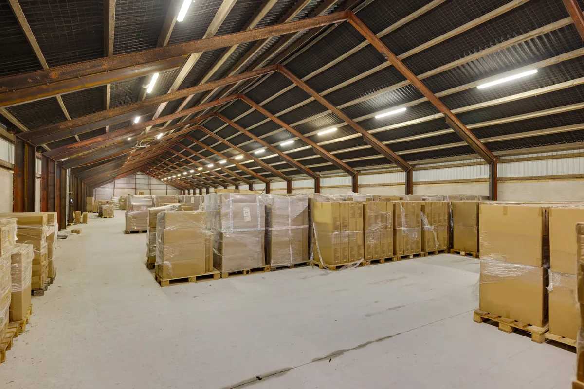 Lagerhal med store lagerkasser på træpæle, stålbjælker og lys. Lofterne er dækket af metal og stålbjælker.