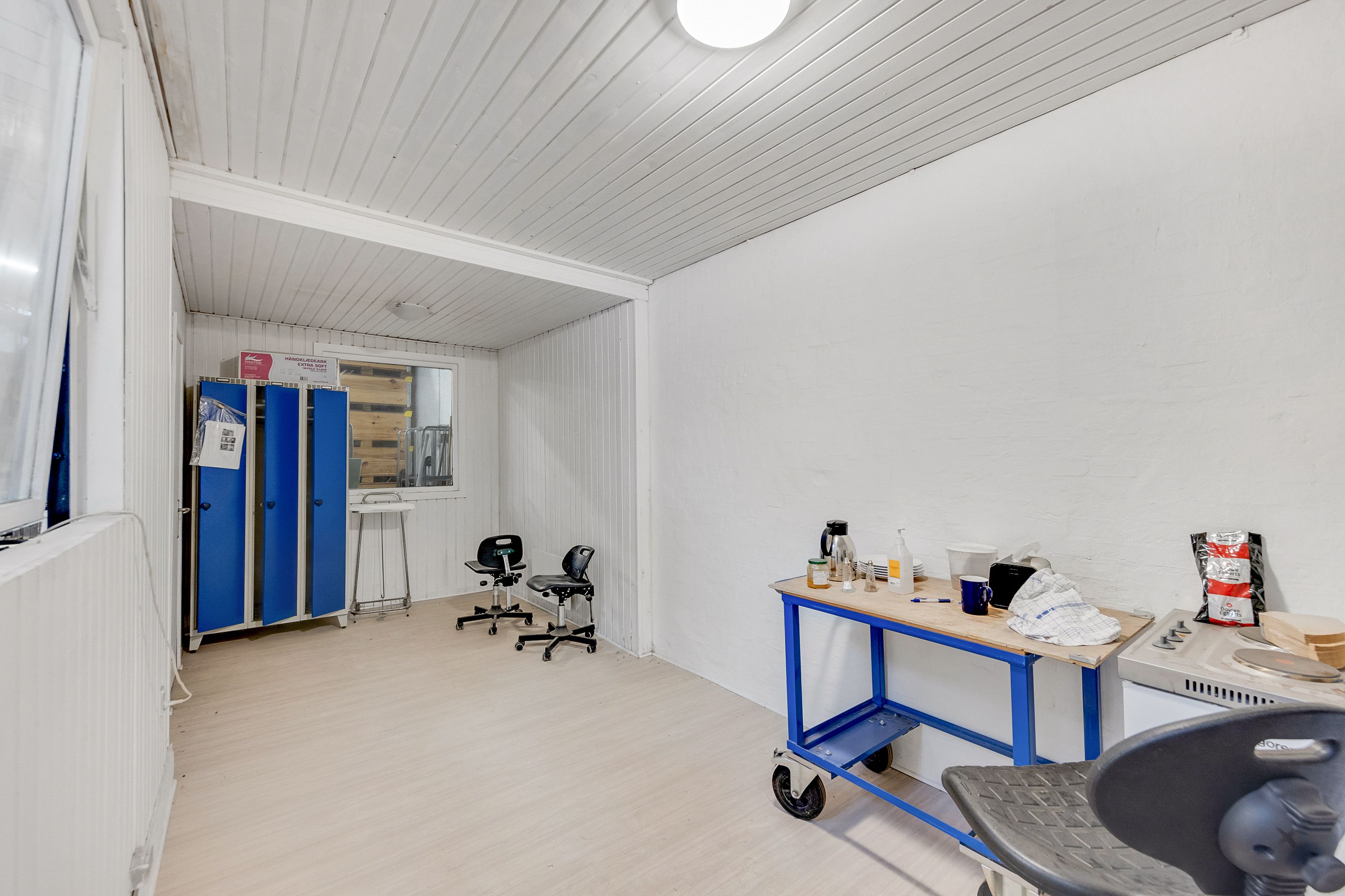 Renset og pænt lokale med to høje blå skabe og en høj skrivebord med flere genstande og en stol med hjul.