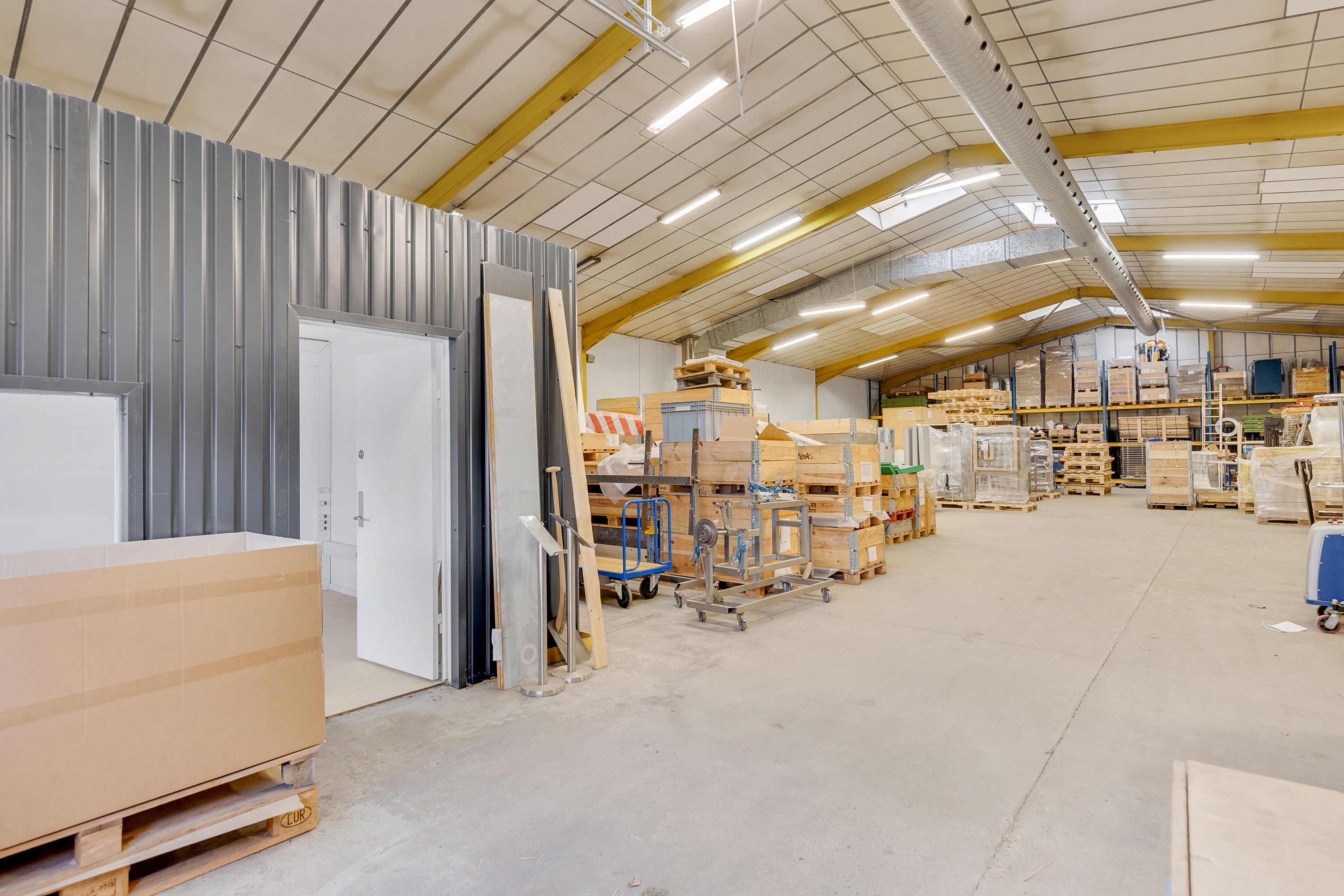 En stor lagerhal med en åben dør og flere kartoner og pallehyller med varer og materialer