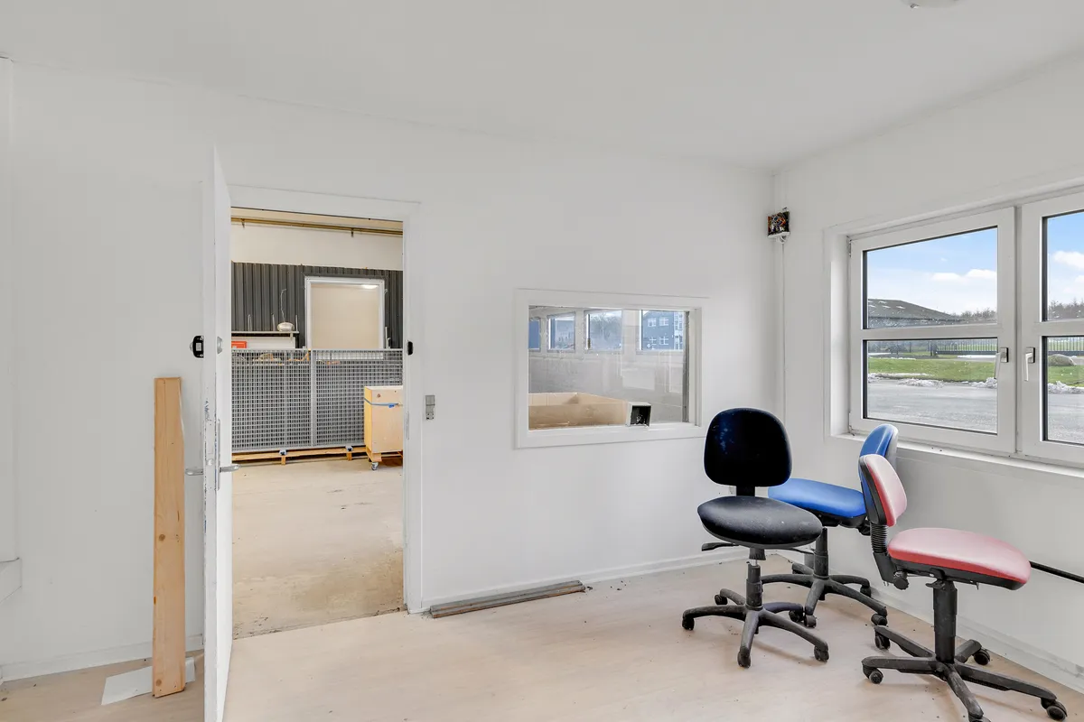 Billede af en tom kontorlokal med hvide vægge og højloft samt trægulv og to vindue på hver side