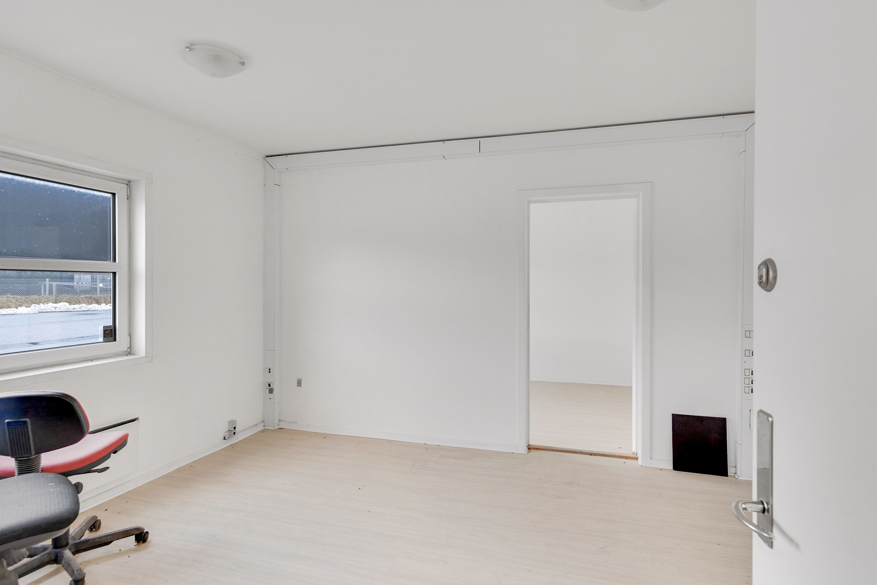 Tomt kontor med hvide vægge, et vindue og et lille kontor med højdepunkter og lysekroner