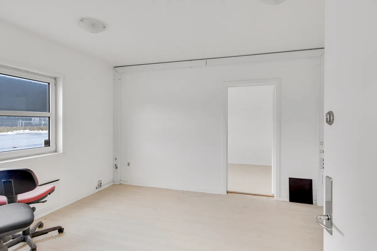 Tomt kontor med hvide vægge, et vindue og et lille kontor med højdepunkter og lysekroner