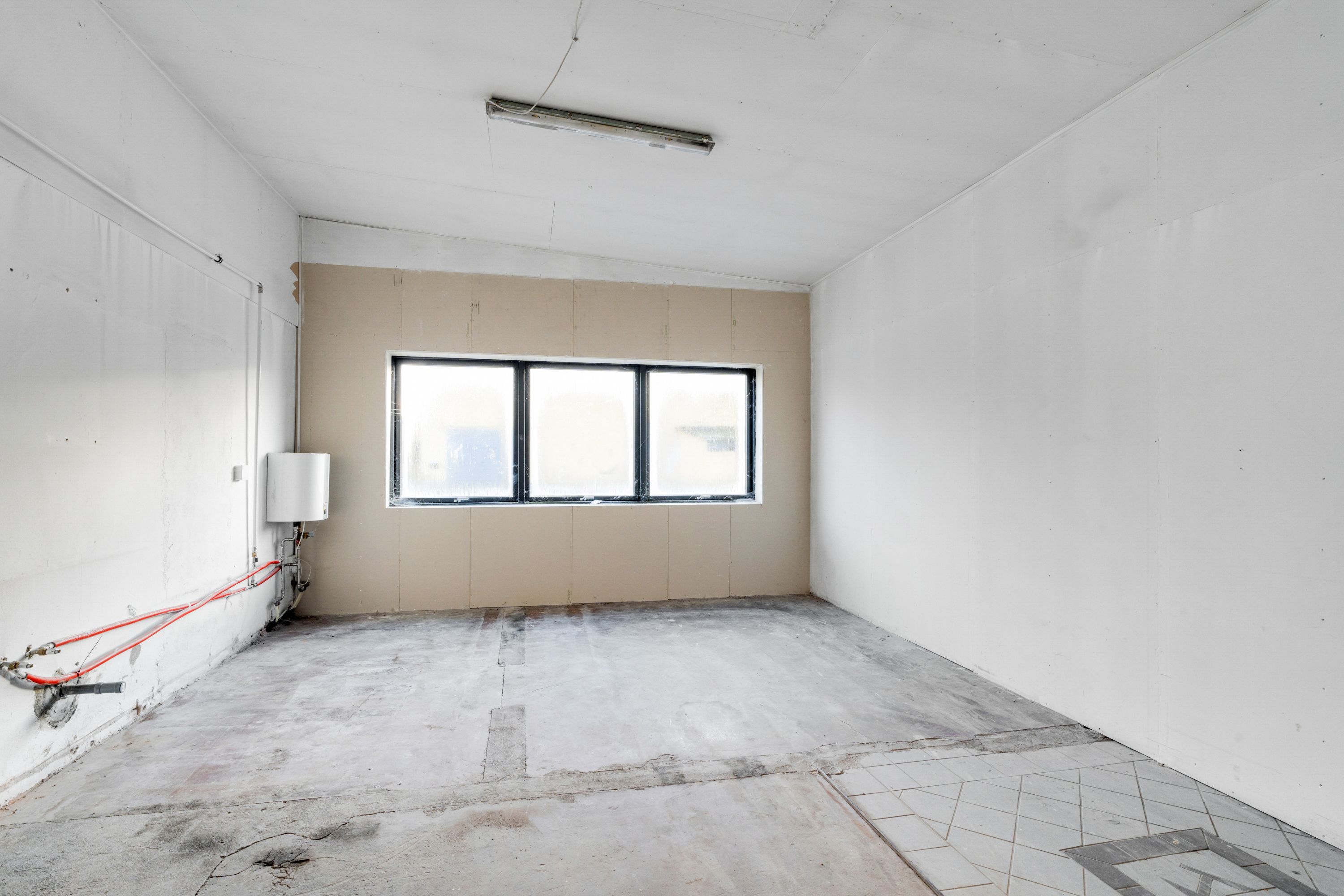 Lejemål med stort tomt rum med vindue og varmeapparat og nye gulvfliser.