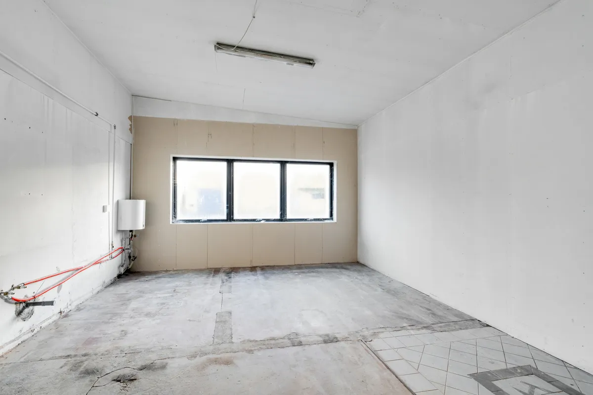 Lejemål med stort tomt rum med vindue og varmeapparat og nye gulvfliser.