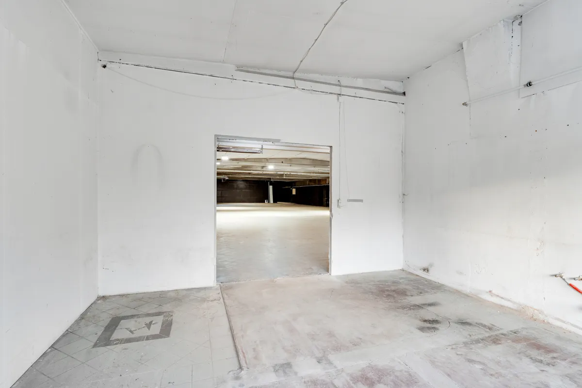 Store tomte med ren, hvid maling og lysegul gulvbelægning med udgang til en bredere, delvis mørkerumlig garage med to