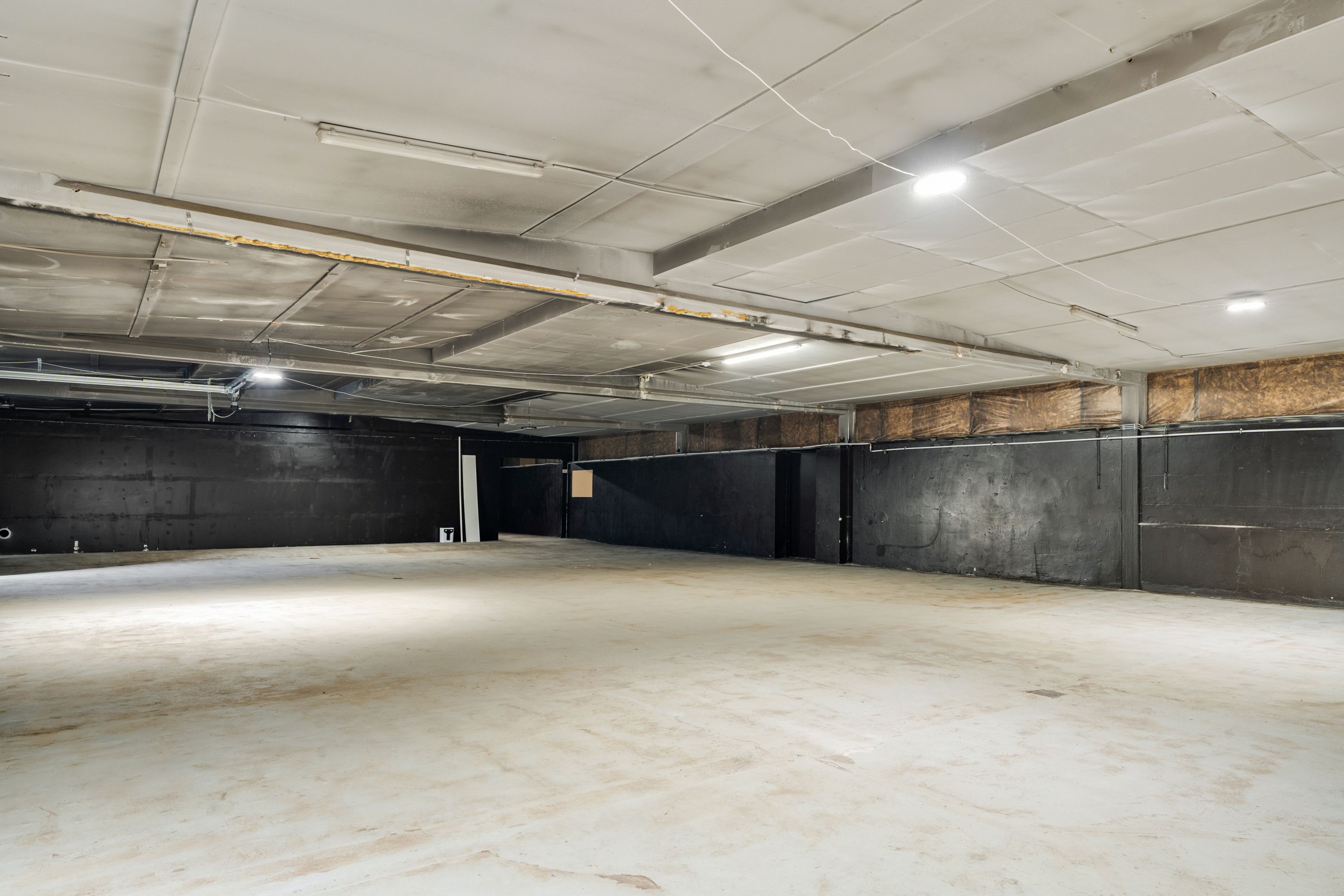 Lejemål med tomme vægge og lysekroner på loftet, med cementgulv og hvide lofter, der giver en åben og neutral atmosfære til