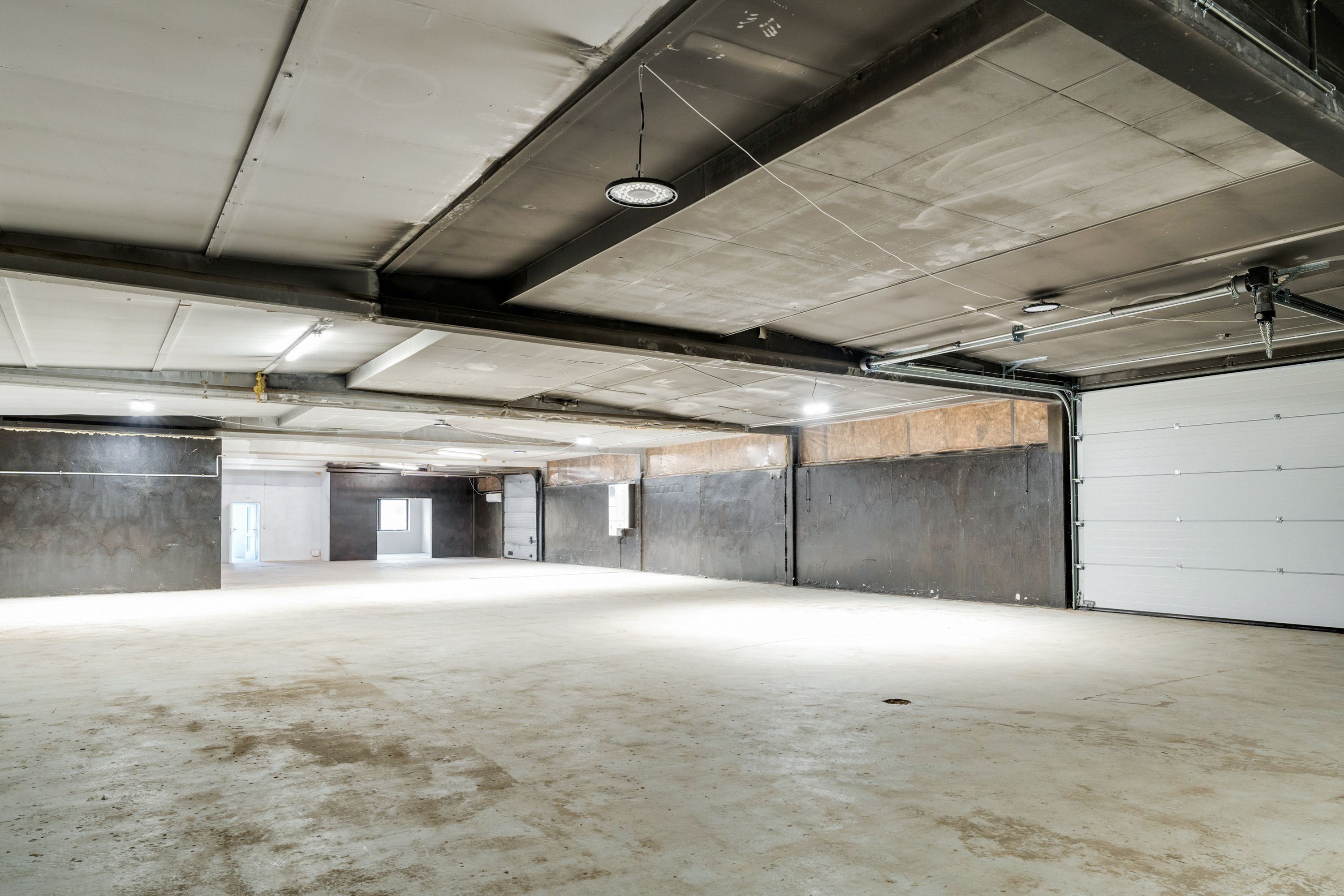 Et stort lager med to garageporte og indgange til højre og venstre samt loftsbelysning og lysekroner