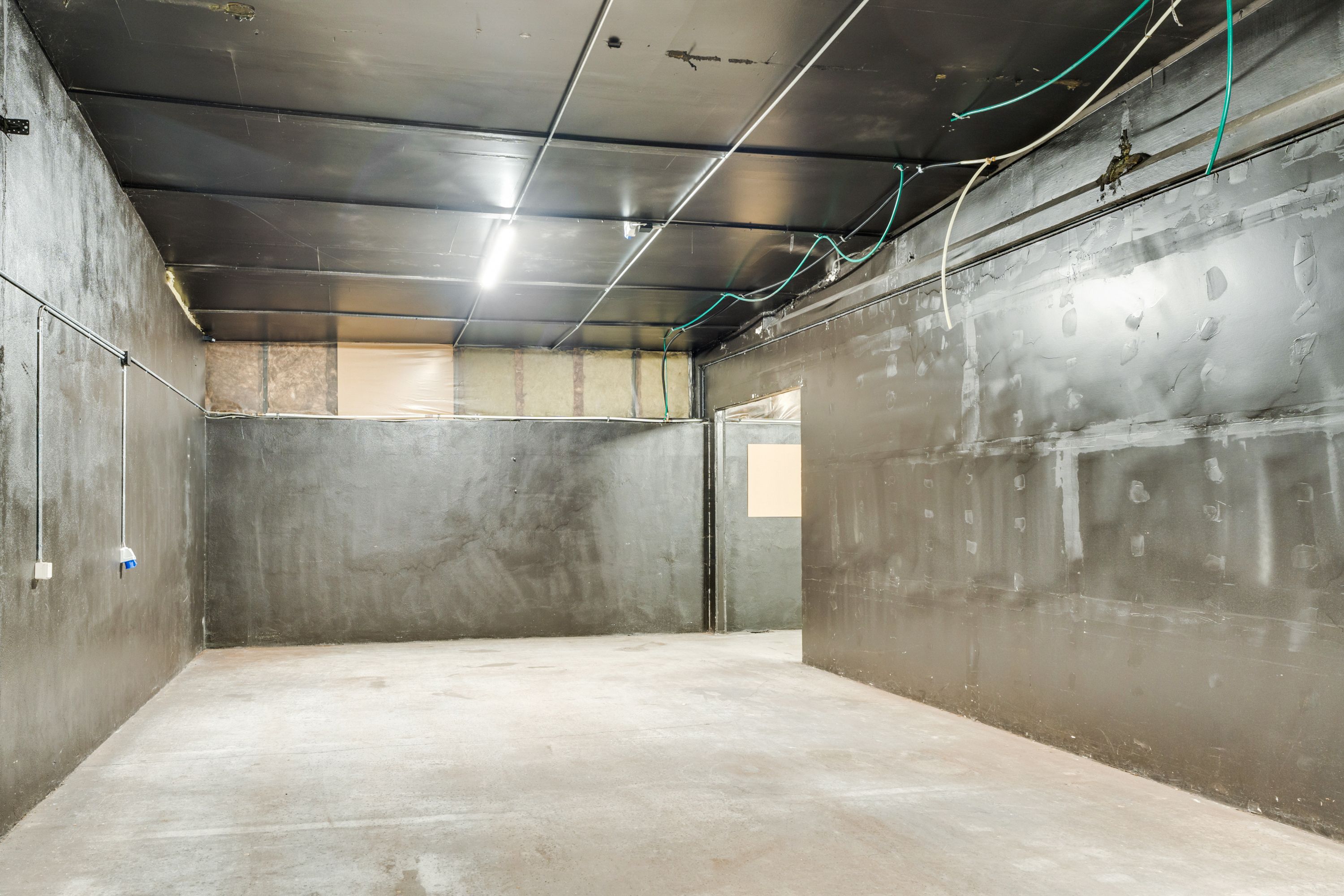 En stor tom lokale med cementgulve og vægge, hvor der er flere ledninger og en dør