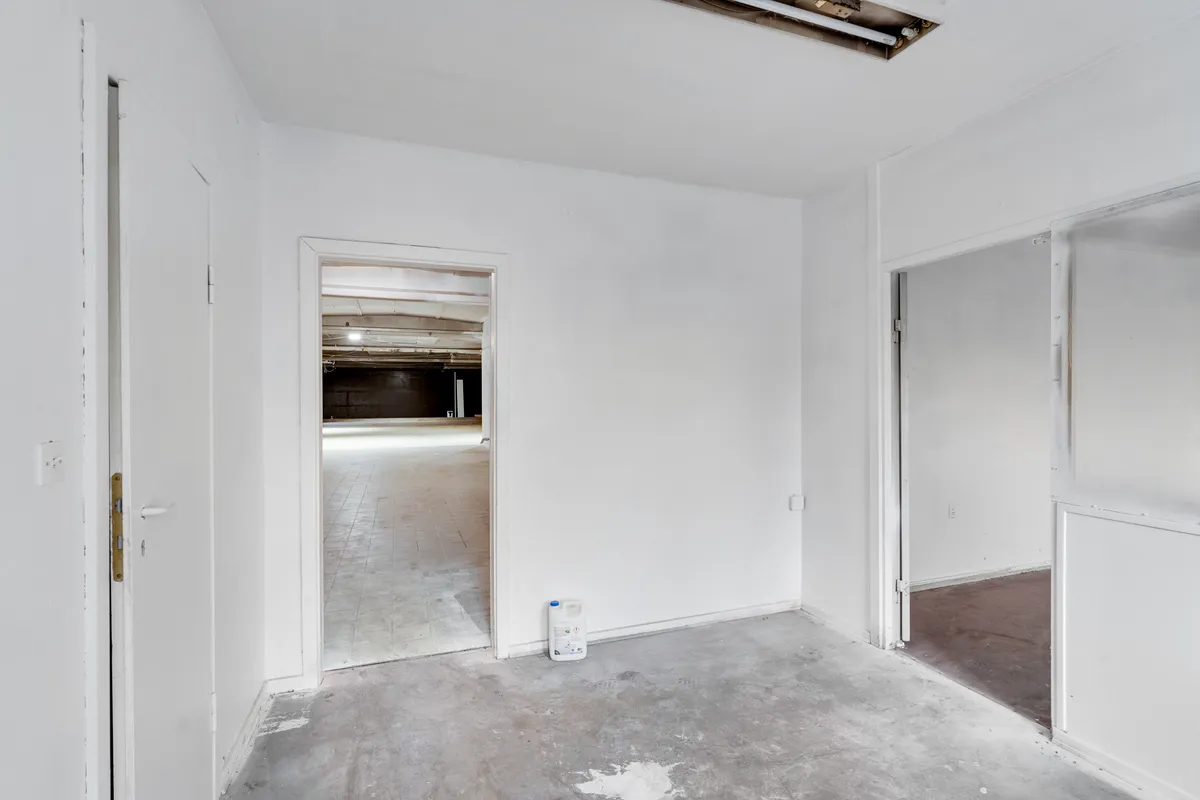 Et tomt lagerrum med to døre og en dør der fører ned til en garage, med en flaske på gulvet og en åben dør til højre