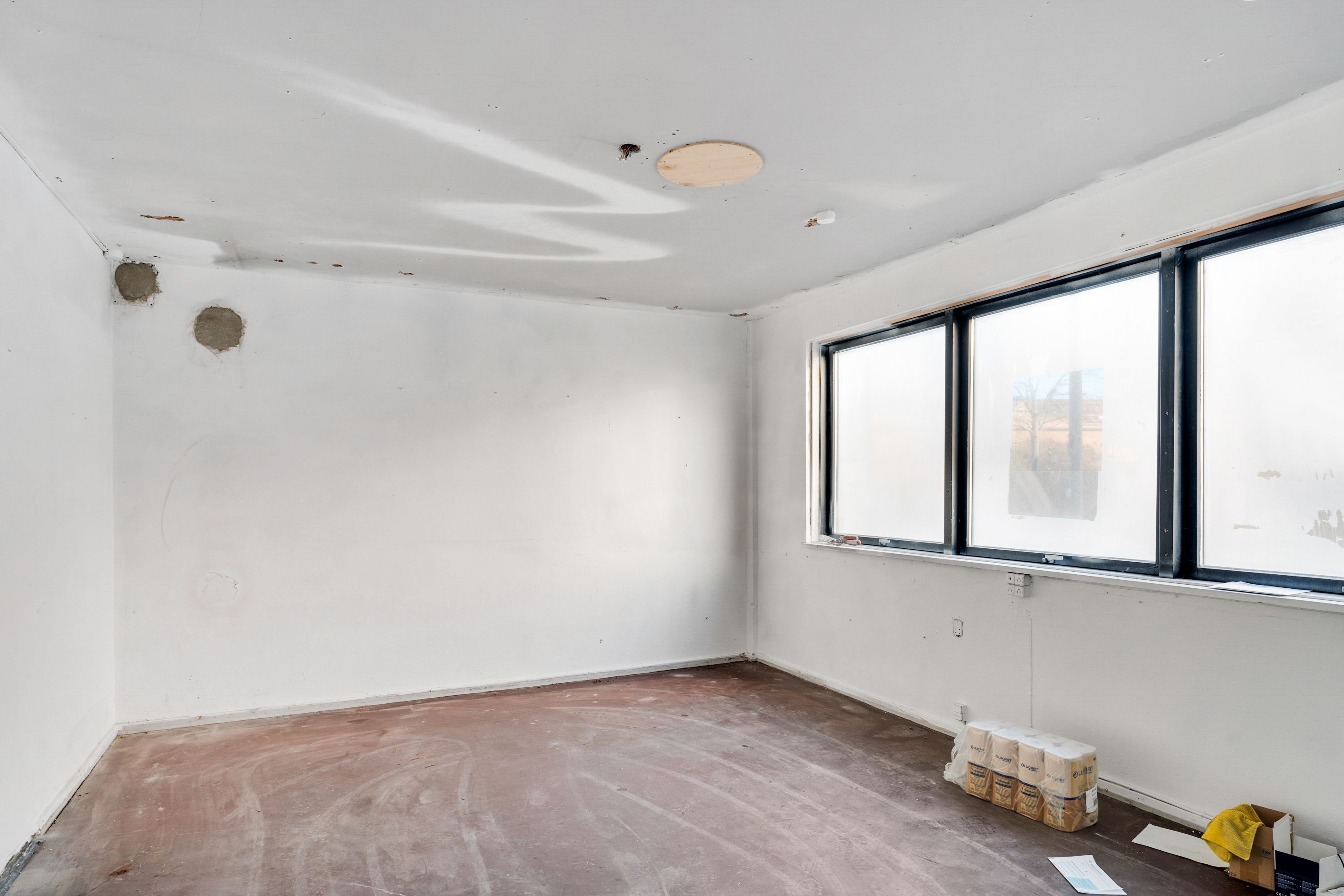 Lejemål med to vinduer og hvidmalede vægge, to ruller toiletpapir, skrald og en klodset gulv med sandfarve