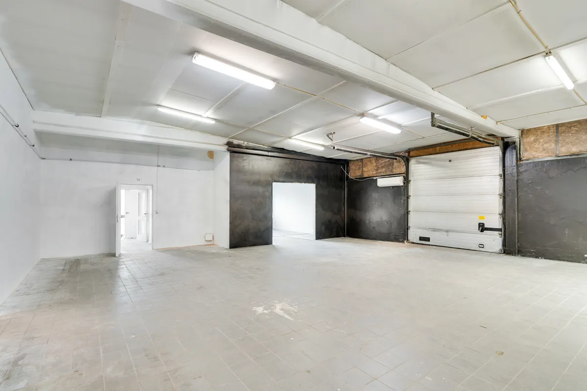Et stort tomt rum med hvide vægge og hvidgule loftsbelægninger, to garageporte og en åben dør