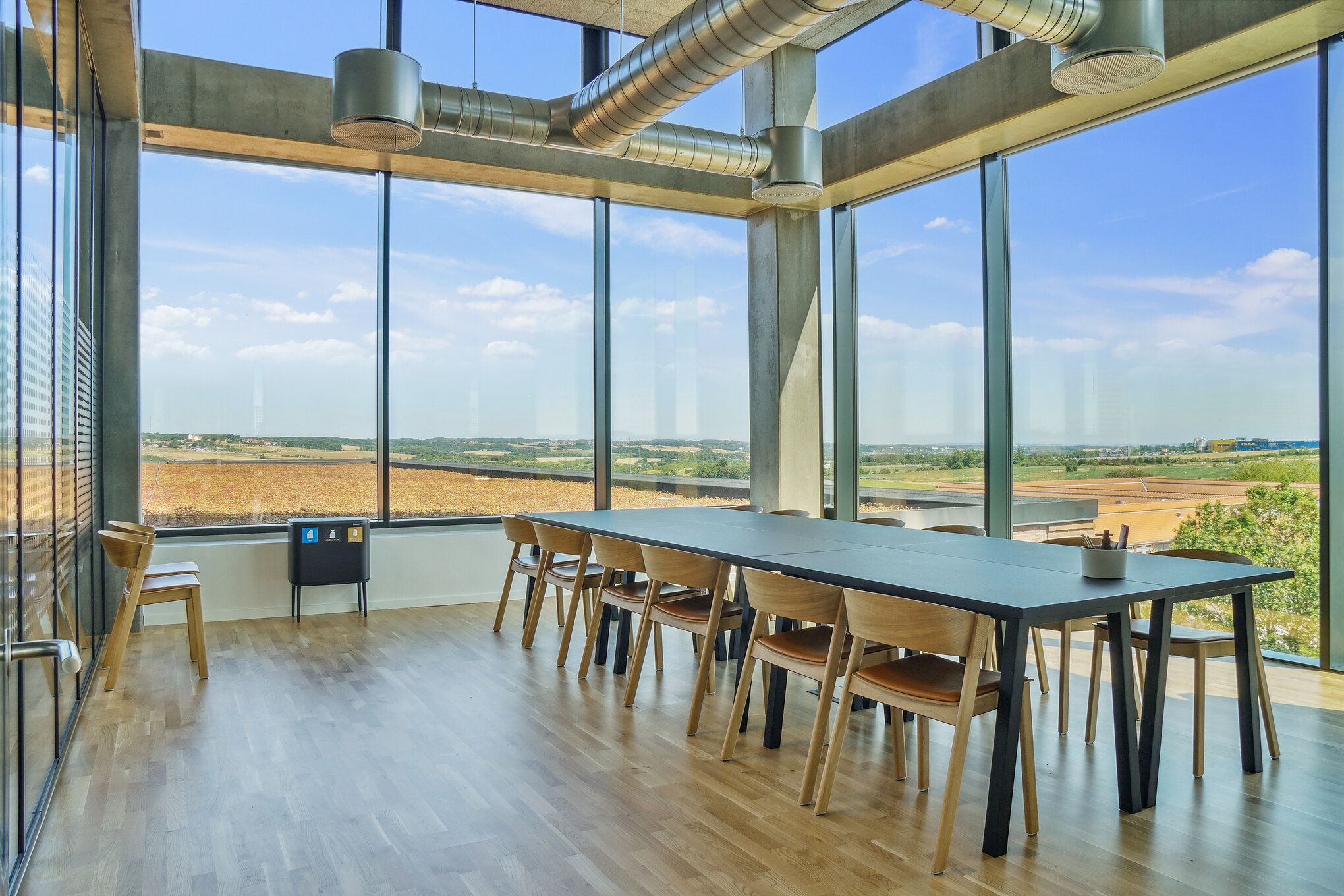 En stor mødehal med store vinduer og et langt bord med stole med udsigt til landskabet og himlen med skyer