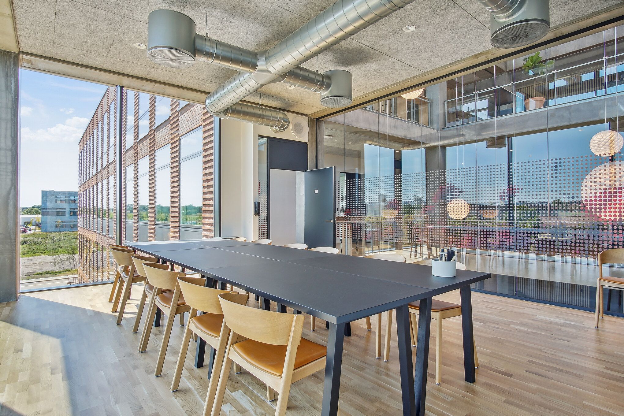 Lys, moderne konferencesal med trægulve, glasvinduer, en lang sort bord og lyse, træstole samt flere lysekroner