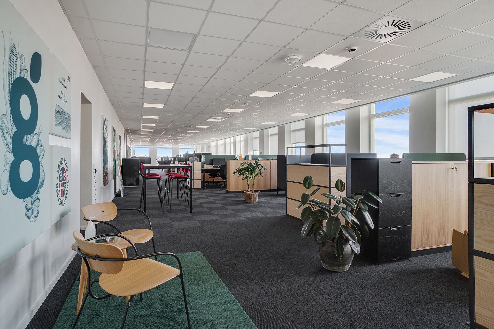 I et moderne kontorområde er der to møbelsæt og en plante i en pot. Væggen er dekoreret med malerier og mærker. Der er flere