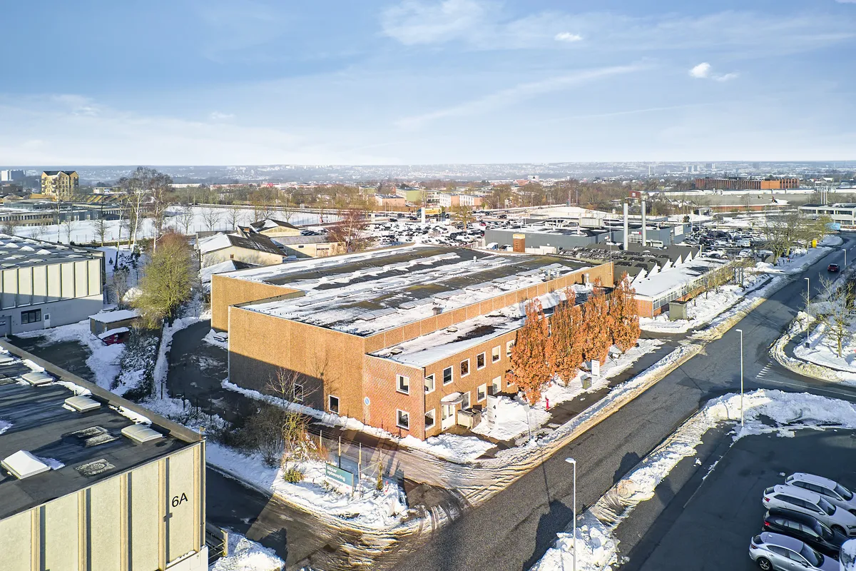 En stor bygning med røde mursten og hvide vinduer i sne. En anden bygning med røde mursten og hvide vinduer. Vejen er dækket